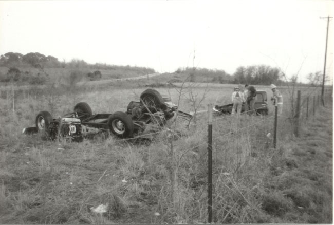 Vintage black-and-white photo of a pickup truck rolled upside down in a field