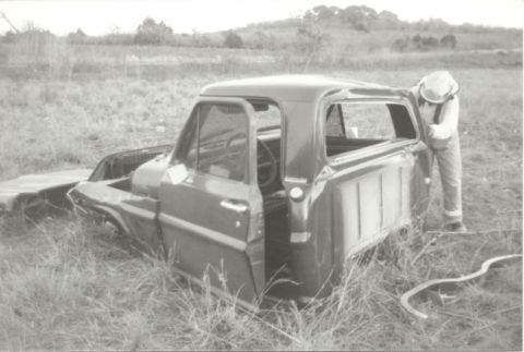1967 Ford F-100 - A 1967 Ford F-100 truck cab and bed sits in a grassy field with a person working on the rear window.
