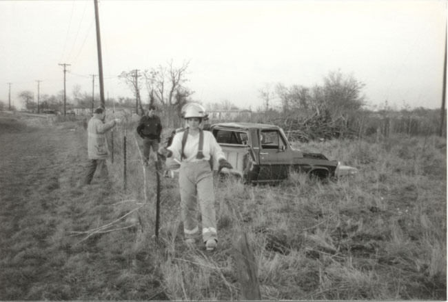 Side view of a dark-colored pickup truck, possibly a 1970s Ford, sitting in a grassy field with its hood open