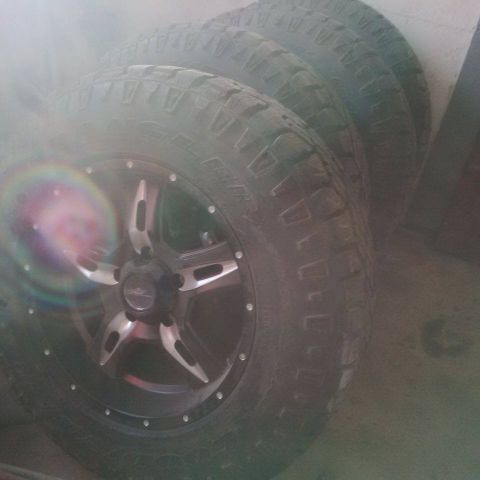 1985 Ford Bronco - A set of four off-road tires and custom rims are shown stacked against a wall.