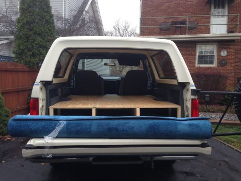 1989 Ford Bronco - Rear view of a white Ford Bronco with a custom storage unit and a rolled-up carpet.