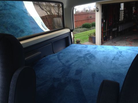 1989 Ford Bronco - The interior of a 1989 Ford Bronco features a custom blue carpeted sleeping area, with a garage visible through the rear window.