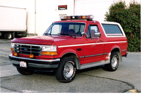 1990 Ford Bronco - This red Ford Bronco, likely a 1992 model, is equipped with an emergency light bar on its roof.