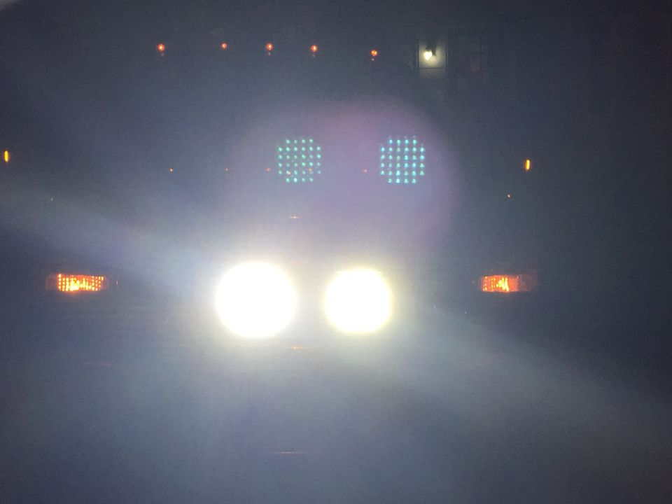 Front of a truck at night, headlights on. Two square green lights above the headlights