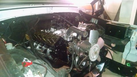 1979 Ford Bronco - Engine bay view with V8 engine components, including headers and fan, in a workshop setting.
