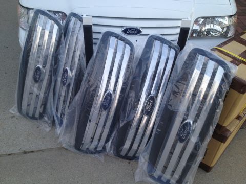 2004 Ford Crown Victoria - Five new Ford grilles are displayed in front of a white 2004 Ford Crown Victoria.