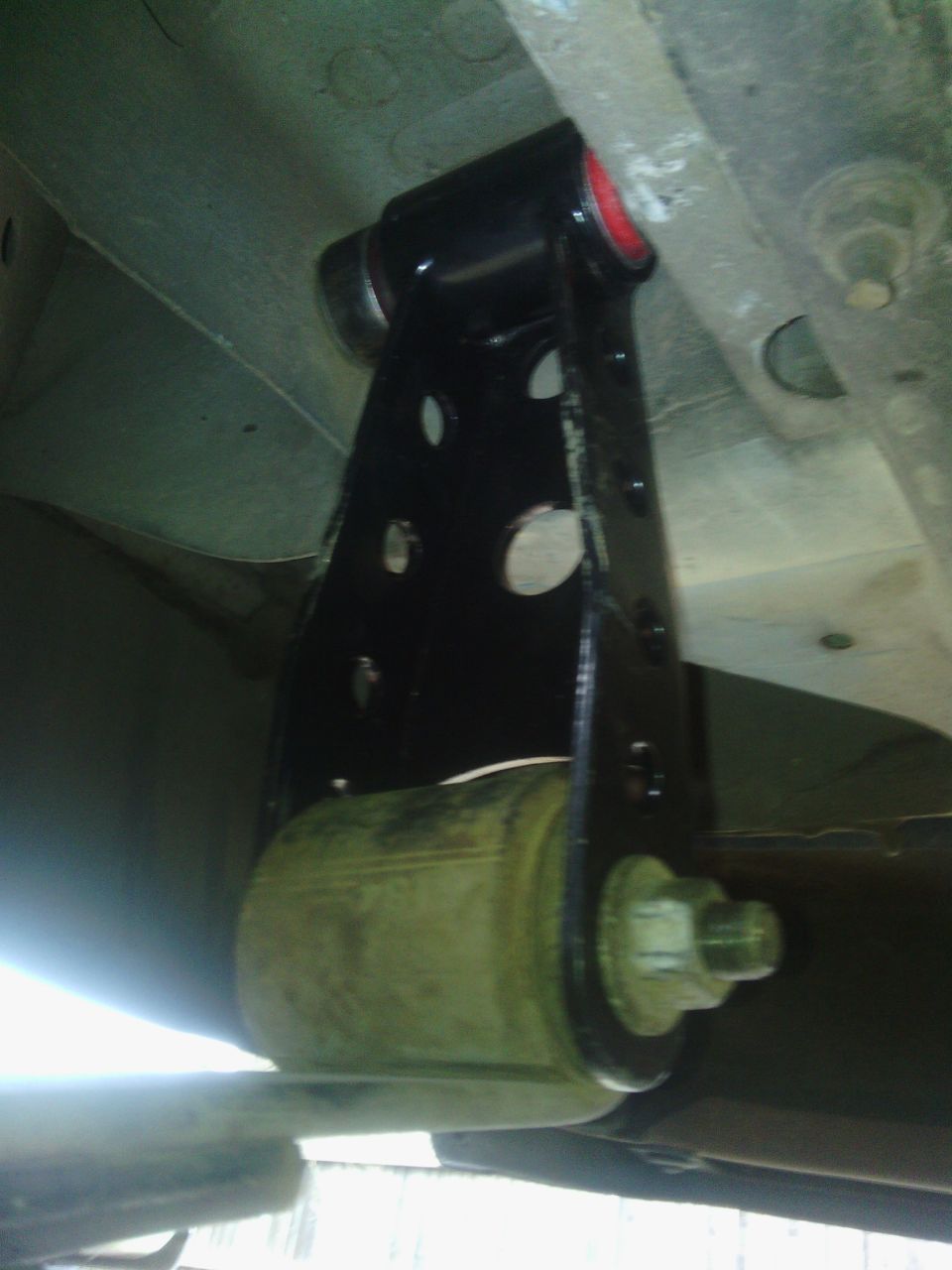 black metal bracket with red bushing attached to a green suspension component