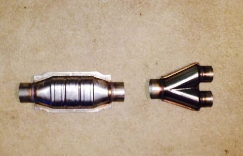 1996 Ford Bronco - Two exhaust system parts, a catalytic converter and a Y-pipe, are laid out on a textured surface.