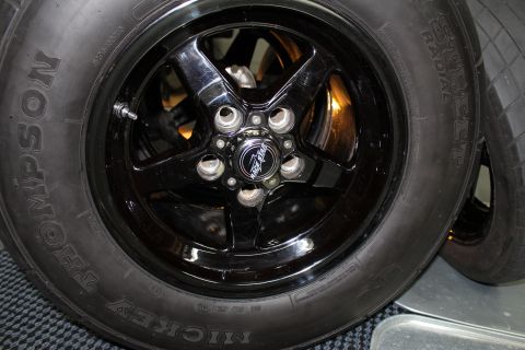 2003 Ford Crown Victoria - front view of a glossy black five-spoke wheel mounted with a Mickey Thompson tire resting on a checkered mat indoors.