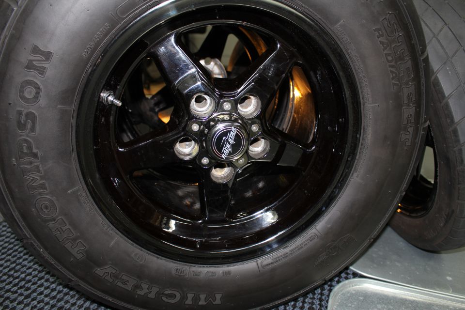 Black five-spoke wheel with Mickey Thompson tire, front view on floor