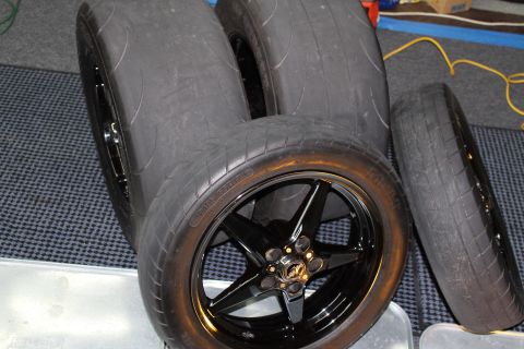 2003 Ford Crown Victoria - black five-spoke drag wheel mounted with a tire staged upright among several other wide tires on a checkered mat.