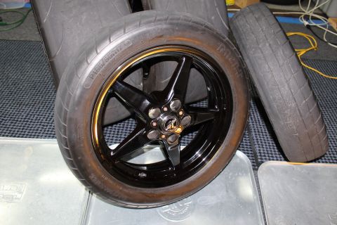 2003 Ford Crown Victoria - single black five-spoke drag wheel mounted with a tire leaning against metal panels on a checkered mat indoors.