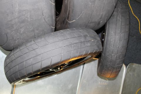 2003 Ford Crown Victoria - pile of wide treaded drag radial tires stacked together on a mat and metal panels indoors.