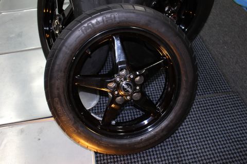 2003 Ford Crown Victoria - black five-spoke wheel mounted with a treaded drag tire lying on a checkered mat, with more wheels behind it.