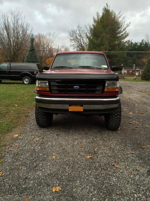 1994 Ford Bronco - This red Ford Bronco is parked outside on a cloudy day, with a black pickup truck in the background.
