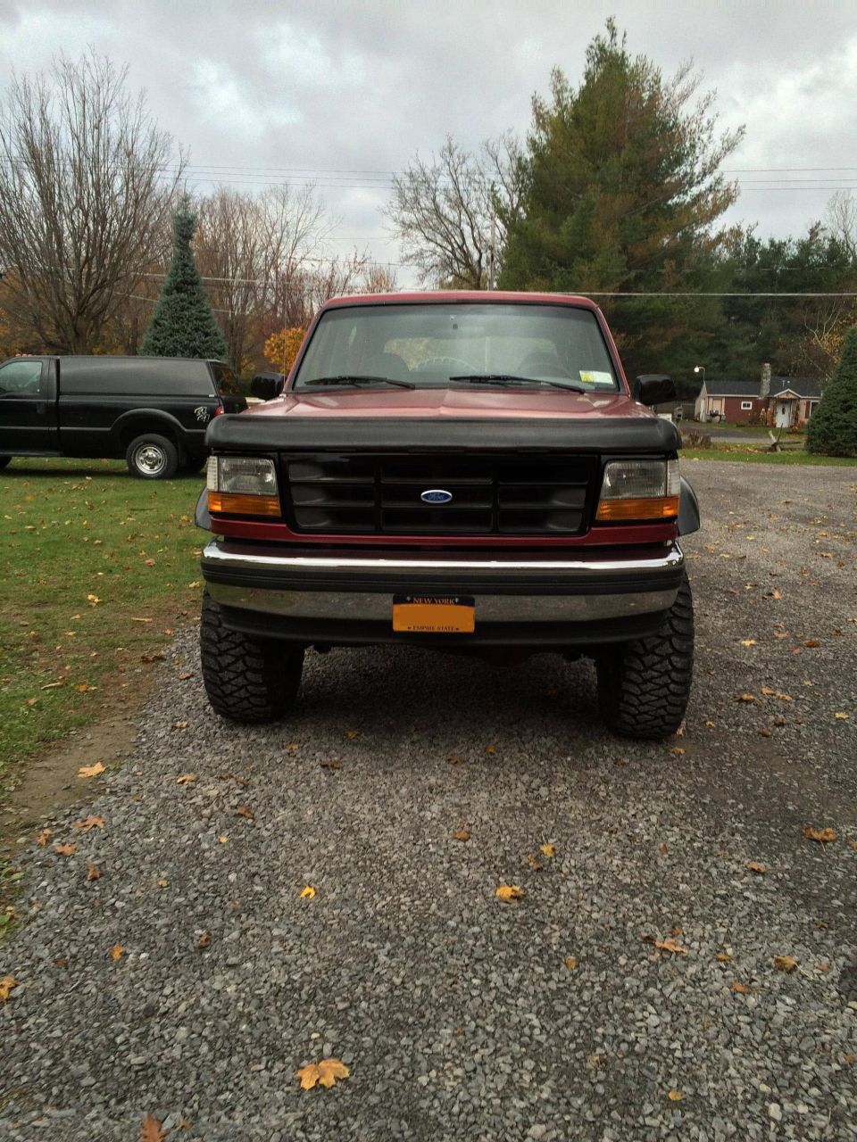 Red Ford Bronco parked on gravel lot, another black truck in background