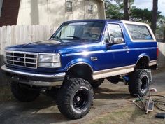 1996 Ford Bronco - This lifted blue Ford Bronco SUV features large off-road tires and a white removable top.