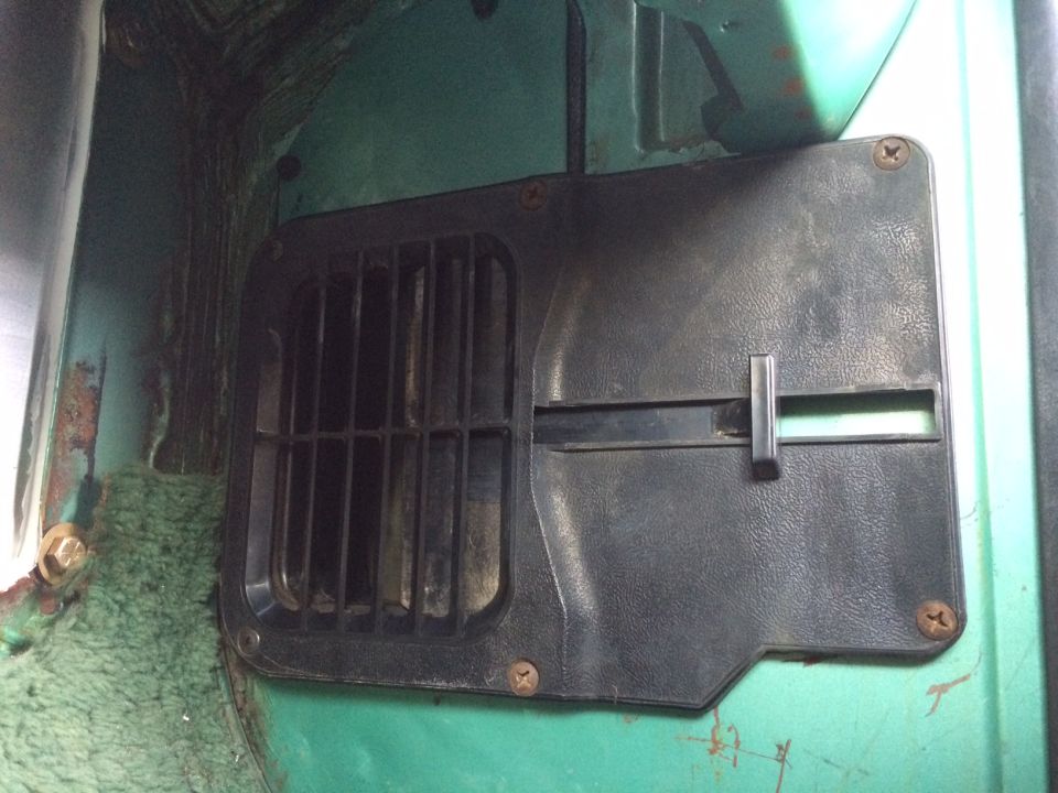 Black plastic vent cover with horizontal slider on green metal surface. Rusty bolts visible