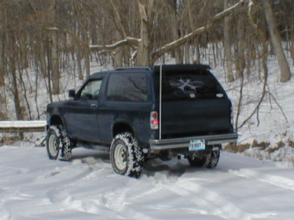 Lifted blue Chevrolet Blazer in snow with white-spoke wheels and mud tires
