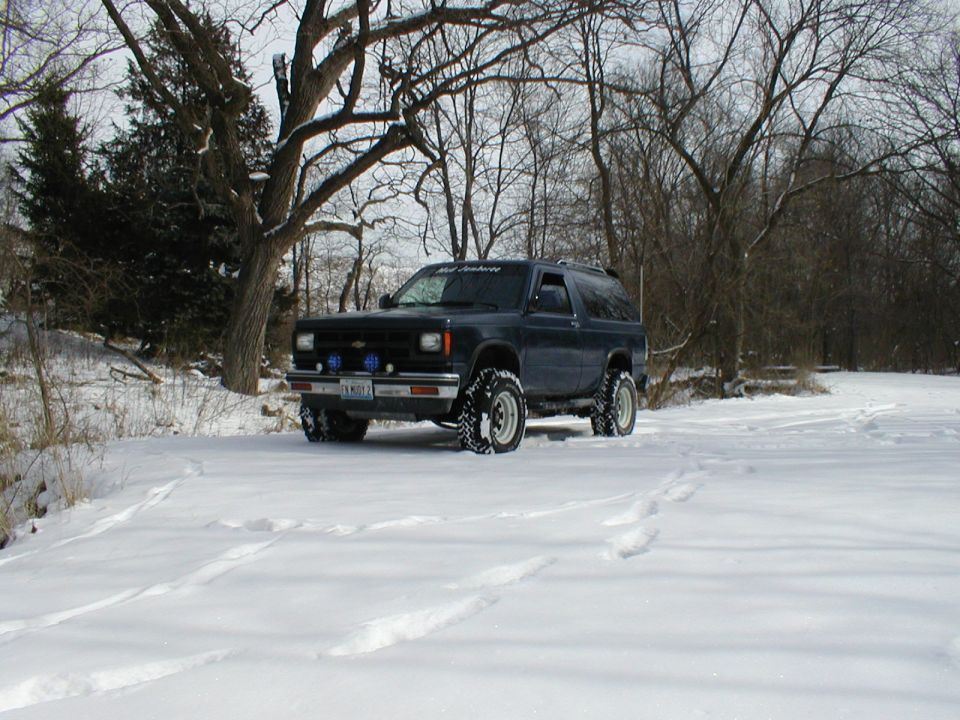 Dark blue lifted two-door Chevy S-10 Blazer with mud tires in a snowy clearing