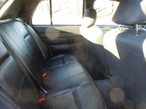 2001 Ford Crown Victoria - The interior of a car shows the back seat and door panel, with black leather upholstery and red seatbelt buckles.