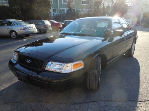 2001 Ford Crown Victoria - The front passenger side of a black Ford Crown Victoria sedan is shown parked on an asphalt surface in front of a building. The vehicle has…
