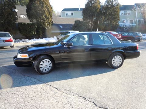 2001 Ford Crown Victoria - The side profile of a black 2001 Ford Crown Victoria is shown parked on an asphalt surface. The car has silver hubcaps and the front passen…