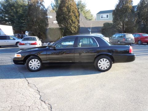 2001 Ford Crown Victoria - The side view of a black Ford Crown Victoria sedan is parked on asphalt. The car has silver hubcaps and a police-style light bar visible on…