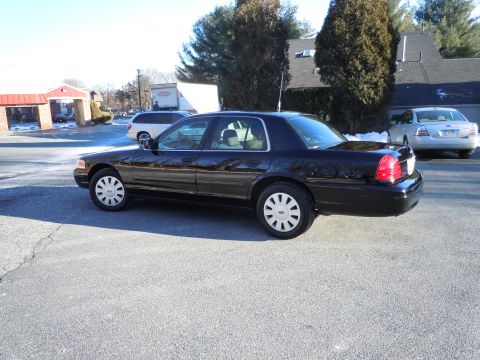 2001 Ford Crown Victoria - The side view of a black 2001 Ford Crown Victoria sedan is shown parked on an asphalt lot. A silver sedan is parked behind it.