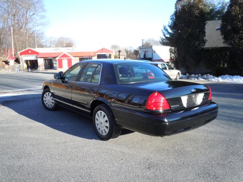 2001 Ford Crown Victoria - The rear passenger side of a black 2001 Ford Crown Victoria is shown parked on an asphalt lot in front of a car wash. The car has a clean e…
