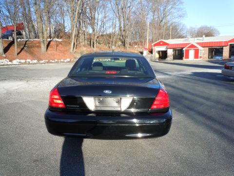 2001 Ford Crown Victoria - The rear view of a black 2001 Ford Crown Victoria sedan is shown parked on an asphalt lot in front of a red-roofed building.