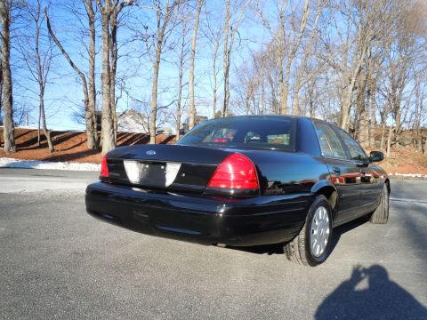2001 Ford Crown Victoria - The rear passenger side of a black 2001 Ford Crown Victoria is shown in a three-quarter rear view. The car is parked on an asphalt surface…