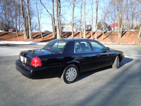 2001 Ford Crown Victoria - The rear passenger side of a black 2001 Ford Crown Victoria is shown from a low angle, parked on an asphalt surface with bare trees and a s…