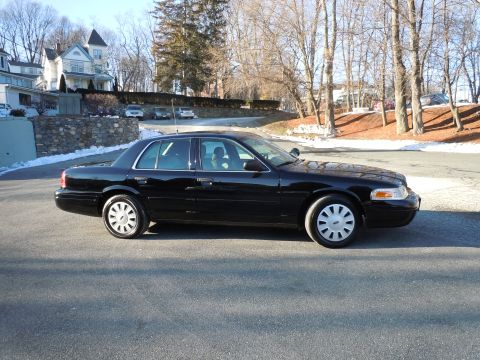 2001 Ford Crown Victoria - A black 2001 Ford Crown Victoria sedan is parked on an asphalt road with snow visible on the side of the road and in the background.