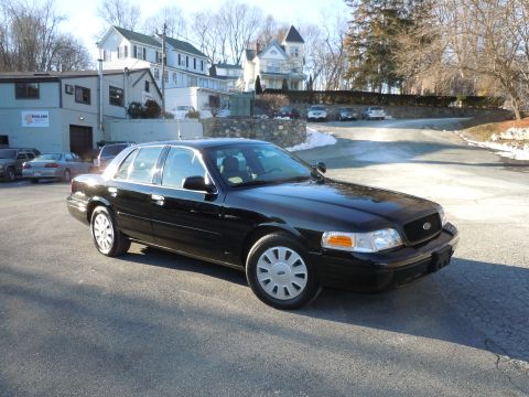 2001 Ford Crown Victoria - A black 2001 Ford Crown Victoria sedan is parked in a lot with a building and trees in the background. The car is viewed from a 3/4 front a…