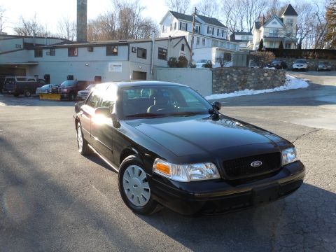 2001 Ford Crown Victoria - A black 2001 Ford Crown Victoria sedan is parked in a paved lot in front of a light-colored commercial building. The car is viewed from a 3…