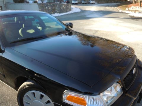 2001 Ford Crown Victoria - The front passenger side of a black 2001 Ford Crown Victoria is shown from a low angle, with the hood and fender in focus. The vehicle is p…