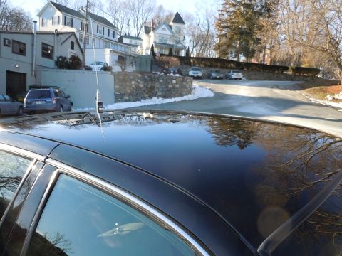 2001 Ford Crown Victoria - The glossy black roof of a sedan reflects the surrounding environment, including bare trees and a winding road with patches of snow. An ant…