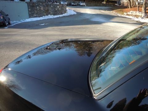 2001 Ford Crown Victoria - The glossy black hood and rear window of a sedan are shown reflecting trees and a street. A portion of the car's body is visible on the lef…