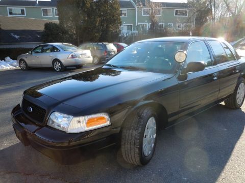 2001 Ford Crown Victoria - A black Ford Crown Victoria sedan is parked in an asphalt lot with a silver sedan and a dark SUV in the background. The front passenger sid…