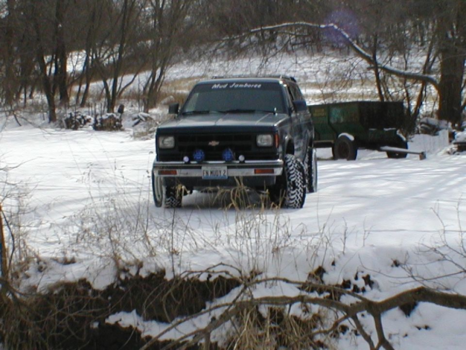 Lifted dark Chevy Blazer in snow with Mud Jamboree windshield banner and four bumper lights