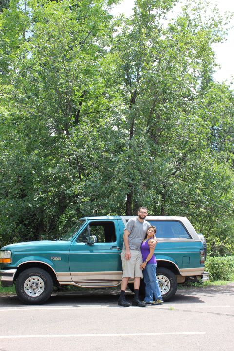 1996 Ford Bronco - A teal and tan 1996 Ford Bronco is parked on a paved surface with a couple standing in front of it. The vehicle is viewed from the side wit…