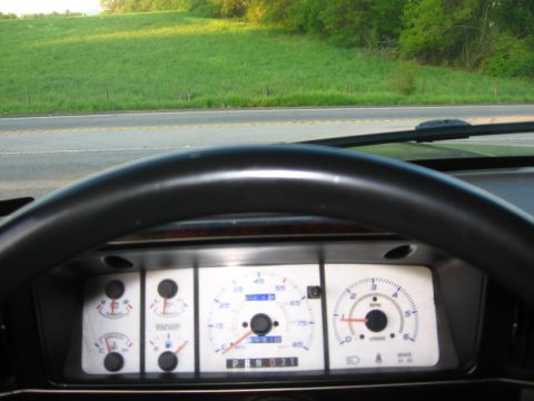1988 Ford Bronco - Interior view of a 1988 Ford Bronco dashboard, showing the steering wheel and instrument cluster. The vehicle is parked on a road with a gr…