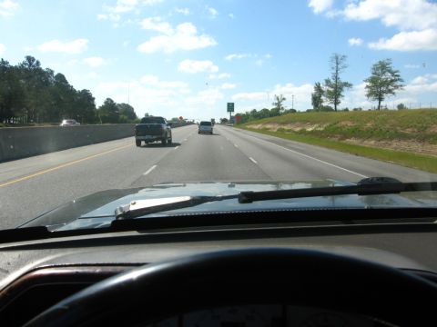 1988 Ford Bronco - View from the driver's seat of a 1988 Ford Bronco on a highway, looking forward over the dashboard and windshield. A dark-colored pickup tr…
