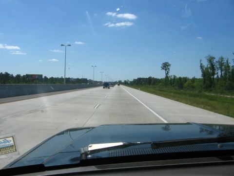 1988 Ford Bronco - The front view of a dark colored vehicle driving on a highway on a sunny day. The vehicle's dashboard and windshield wipers are visible in…