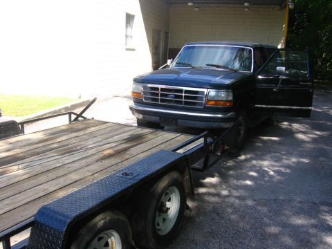 1988 Ford Bronco - A black Ford SUV is parked next to a wooden trailer. The driver's side door of the SUV is open, and the vehicle is hitched to the trailer.