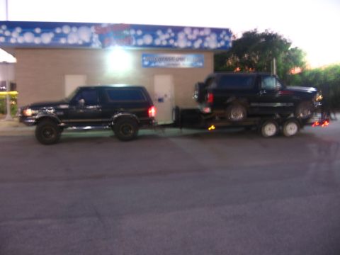 1988 Ford Bronco - A black Ford Bronco is parked in front of a car wash, and another black Ford Bronco is loaded onto a trailer behind it.