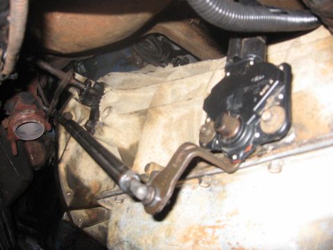 1988 Ford Bronco - Underneath view of a vehicle's transmission linkage and shifter mechanism. A black plastic shifter assembly is visible, connected to a meta…