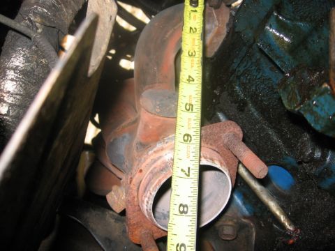 1988 Ford Bronco - A yellow measuring tape is positioned next to a rusty exhaust manifold and a portion of a blue engine block. The tape shows measurements fr…