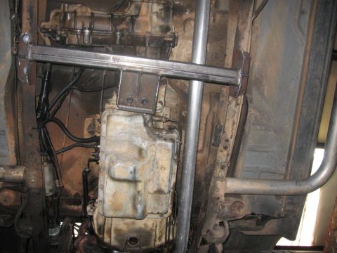1988 Ford Bronco - Underneath view of a vehicle's transmission and exhaust system, showing a custom metal bracket installed near the transmission crossmember…